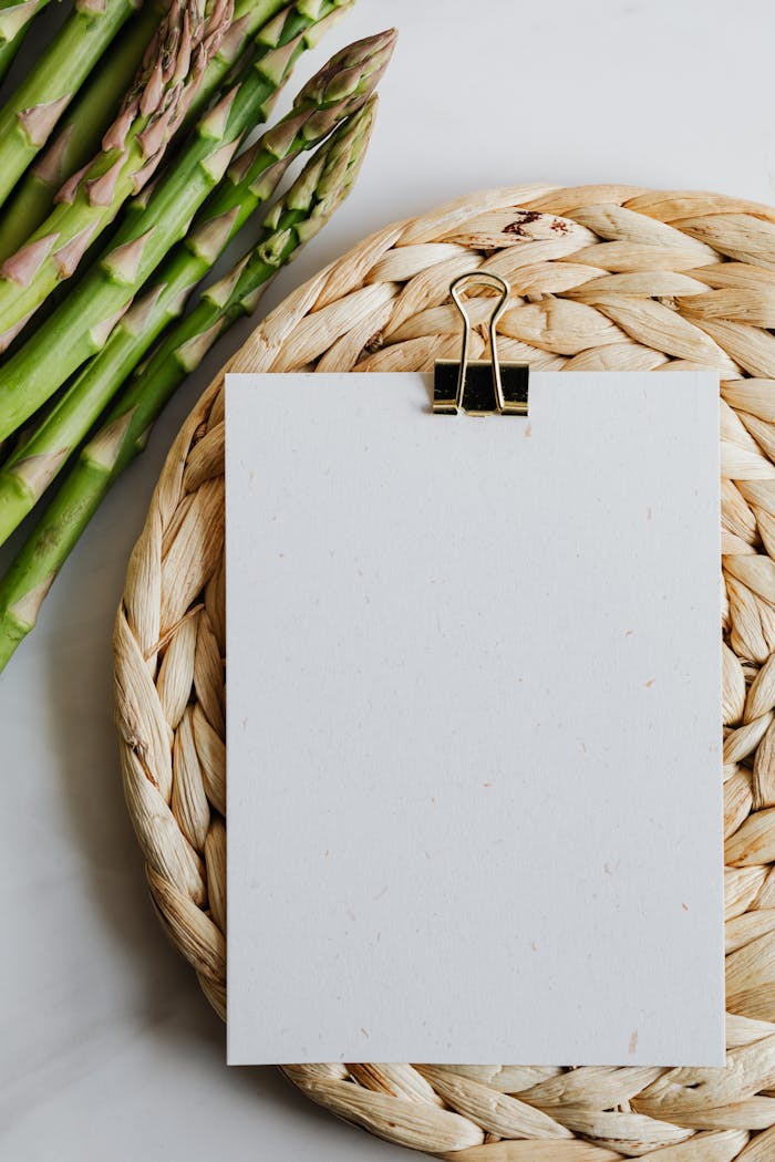 Top view of fresh asparagus next to a blank note on a woven mat. Perfect for culinary themes.